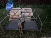 Two metal patio chair frames and stacked cushions on grass
