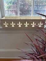 Full view of cream metal window box on windowsill showing fleur-de-lis cutouts