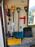 All three items hanging: Worx trimmer, Garant pusher, generic shovel