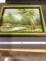 Front view of framed landscape painting with measuring tape indicating size