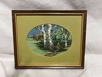 Front view of framed needlepoint showing landscape subject, oval mat, wood frame with gold trim