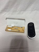 Front view of Google Nest Hello doorbell with accessory box containing mounting bracket and pin tool