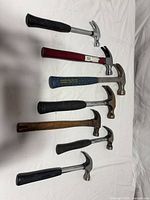 Seven claw hammers laid out to show variety of handles and heads