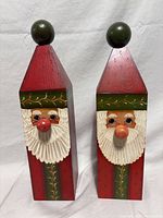 Front view of both wooden Santa figurines showing carved faces and painted details