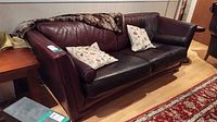 Full front view of burgundy leather sofa with throw pillows and fur throw, shows overall style and wear