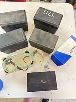 Four black plastic goggle cases, Wilson case, U.S. Safety cardboard box, one green goggle and one clear goggle visible