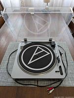 Turntable open showing platter, tonearm, RCA cable