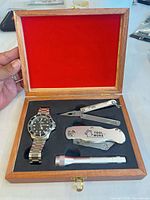 Open wood box showing wristwatch, multi-tool, utility knife, flashlight set in foam