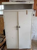 Front view of off-white metal cabinet with double doors, latch and top shelf
