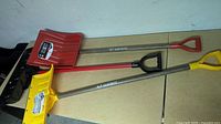 Three snow shovels laid out showing handles and coloured blades
