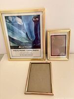Three gold/brass metal frames—8×10 wrapped, two 5×7—front view