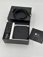 Apple TV HD box opened with device, remote, HDMI cable and booklet visible