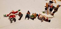 Seven miniature Christmas figures laid out: Santa, five children/elf figures, snowman scene
