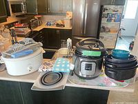 Overview of all items on countertop including Instant Pot, West Bend slow cooker, black pots, mixing bowls, dish rack, trivet, utensils