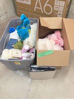 Grey plastic tote and open cardboard box filled with plush animals and books