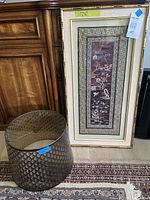 Full view of framed silk embroidery leaning against cabinet