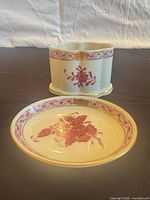 Front view of oval dish and matching toothpick holder showing decorative motifs and gilt trim