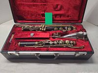 Open case showing bass clarinet joints, neck, bell, mouthpiece, ligature, cap in red plush interior