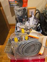 Plastic bin with face shield, drill bits, wire connectors, conduit hose, cords