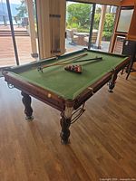 Full view of 8 ft pool table with cues, balls and rack on playing surface