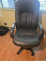 Front view of black faux leather office chair showing seat, armrests and swivel base