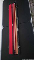 Pool cue disassembled in black hard case, red lining visible