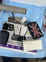 All items grouped: router box, Fujifilm camera, camera case, Linksys extender, UK flag phone pouch, jewellery display stand