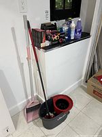 Overview showing broom, dustpan, spin mop bucket and assorted cleaners on ledge