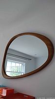 Front view of mirror on wall showing organic shape and teak frame