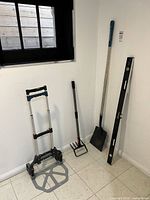 Full group view of hand truck, shovel, fork, and level leaning against wall
