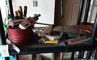 Overview of assorted hand tools in red metal tub on shelf