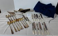 Full set laid out: spoons, knives, forks, cake server, crumb brush and storage roll