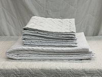 Stacked coverlet and four folded shams showing quilting pattern and overall set