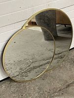 Two round gold-trim mirrors leaning on wall, showing size difference