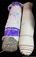 Rolled carpet padding in labeled bag beside rolled taupe carpet