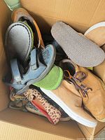 Top view of box showing multiple shoe styles including blue sport sandal, green slip-on, tan sneaker, leopard flat etc.
