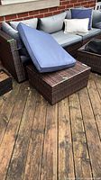 Square brown resin wicker ottoman with blue cushion resting on top
