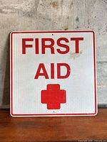 Front view of metal First Aid sign with red lettering and cross