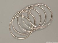 All five silver bangles laid flat showing twist pattern