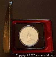 Closed black presentation case open showing encapsulated coin in red flock interior