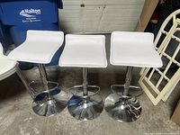 Front view of three white faux leather bar stools showing seats, height, and chrome bases