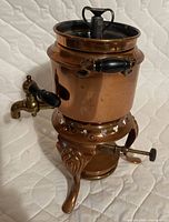Front view of assembled copper and brass percolator showing spout, handles, stand, burner knob