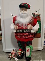Full view of tall Santa doll with golf bag and clubs, two small figurines and mini golf bag at feet
