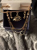 Front view of brooch hanging on gift box showing evil eye charm, star charms, layered chains, pearls