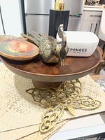 Overall grouping of items on cake stand with brass butterfly trivet and placemats