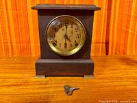 Full view of wooden Sessions mantel clock with key in foreground