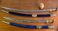 Full view of both curved talwar swords with scabbards and brass hilts