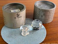Both Swarovski crystal pieces with their cylindrical boxes and felt pad displayed