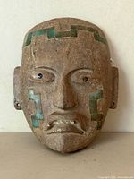 Front view of brown stone mask with turquoise inlay and facial features