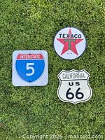 three metal signs laid on grass: Texaco, Interstate 5, California US 66